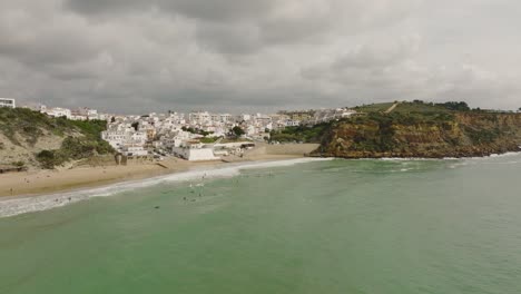 Aerial-shot-of-surfers-waiting-for-waves-at-a-beach-along-the-Atlantic-Ocean-in-Portugal-underneath-a-cloudy-sky
