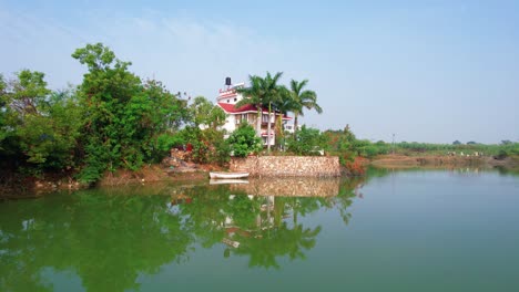 Tropical-White-House-reflected-in-the-river-surrounded-with-Palm-Trees-and-Natural-Vegetation-in-Gujarat,-India