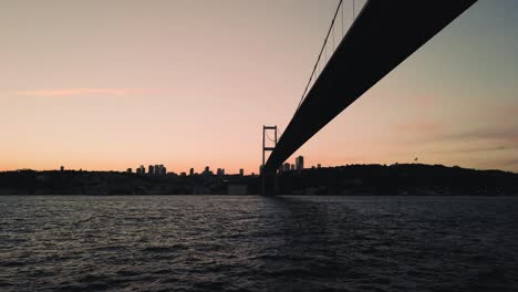 View-of-the-Martyrs-Bridge-from-a-boat-moving-on-the-waters-of-the-Bosphorus,-against-the-background-of-a-cloudy-sunset-sky