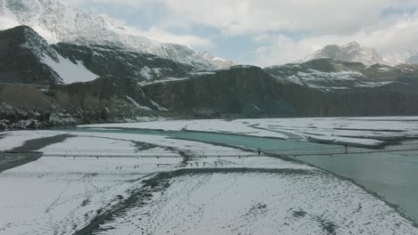 Luftaufnahme-Von-Menschen,-Die-Die-Hussaini-hängebrücke-über-Den-Fluss-Hunza-Gegen-Die-Schneebedeckte-Landschaft-überqueren