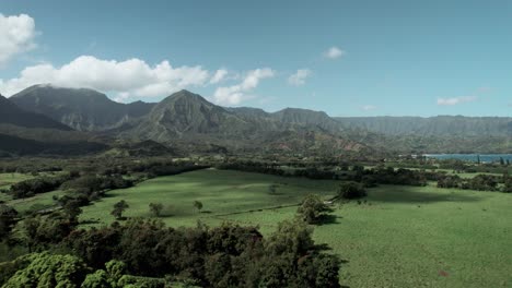 Fluffy-clouds-pass-across-tropical-mountains-above-Hanalei-Bay-and-Princeville,-Kauai,-aerial
