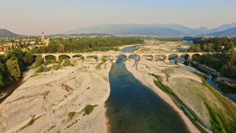 Aerial-drone-view-of-the-river-Piave-in-Italy,-wit-the-old-bridge-crossing-it,-architecture-of-the-'900