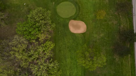 Aerial-View-Of-Green-Golf-Course-Next-To-A-Road-With-Cars