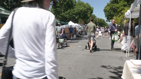 Father-carrying-a-baby-stroller-in-a-local-street-market-full-of-people-and-street-stalls