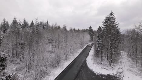 Furgoneta-Conduciendo-Por-Una-Carretera-Aislada-A-Través-De-Un-Impresionante-Bosque-Cubierto-De-Nieve-En-El-Campo-Rural-De-Alemania-Occidental,-Europa