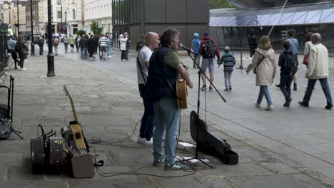Seitenansicht-Von-Zwei-Männlichen-Straßenmusikanten,-Die-Am-7.-Mai-2022-Gegenüber-Der-Cutty-Sark-In-Greenwich-Gitarre-Spielen-Und-Singen