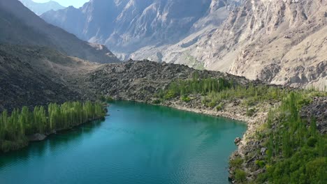 aerial-drone-of-a-unique-glacier-blue-lake-called-Upper-Kachura-Lake,-surrounded-by-a-green-forest-in-the-mountains-of-Skardu-Pakistan-on-a-sunny-summer-day