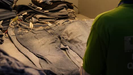 Worker-Checking-Stack-Of-Denim-Jeans-Under-Light-In-Factory-In-Pakistan