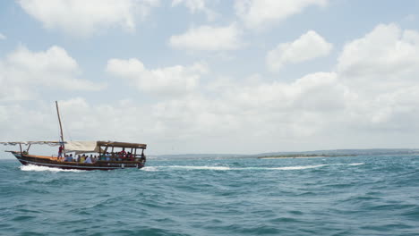 Wooden-dhow-boat-with-passengers-cruising-on-sea-waves,-Zanzibar