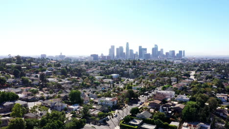 Beautiful-drone-shot-flying-high-above-neighborhoods-of-Los-Angeles,-California-showing-the-city-skyline,-palm-tree-lined-streets,-homes-and-driving-cars
