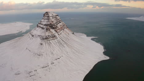 Filmische-Aufnahme-Des-Massiven-Kirkjufell-berges,-Schneebedeckt-Und-Kaltes-Fjordwasser-Im-Hintergrund-Während-Des-Wintertages