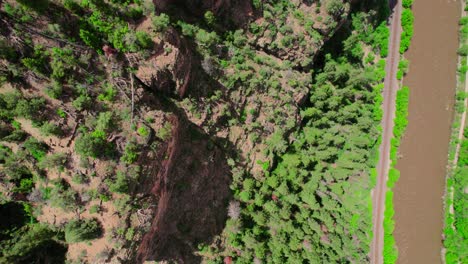 Aerial-Footage-Hovering-Over-Steep-Gorge-Canyon-Cliffside-Covered-In-Bright-Healthy-Green-Trees-Near-Brown-Flowing-River-In-Glenwood-Canyon-Colorado-USA