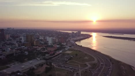 Aerial-Flyover-Of-Asunción-Bay-And-The-Paraguay-River-While-The-City-Is-Being-Lit-With-The-Sun-Setting