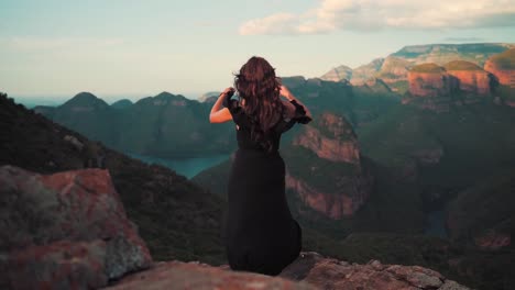 Young-woman-in-black-dress-enjoying-the-view-of-a-valley-during-sunset,-huge-canyon-landscape-visible-in-background