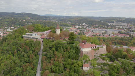 Aerial-view-wide-orbit-around-historic-hilltop-Glokenturm-tower-on-Graz's-Schloßberg-with-views-across-the-city-skyline