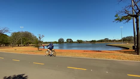 slow-motion-footage-of-a-cyclist-riding-along-a-large-lake-in-brasilia-city-park-and-enjoying-a-summer-day
