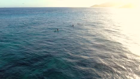 Statische-Drohnenaufnahmen-Von-Zwei-Surferinnen-Und-Einem-Surfer,-Die-Während-Des-Sonnenuntergangs-In-Hawaii-Auf-Wellen-Warten