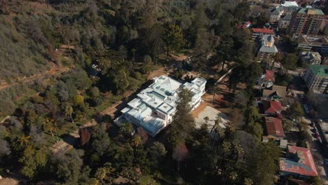 Aerial-orbit-over-Quinta-Vergara-Palace-and-Park-surrounded-by-tree-forest,-Viña-del-Mar-hillside-city-buildings,-Chile