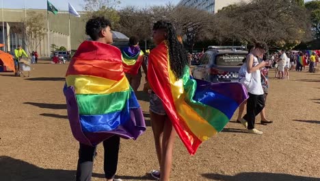 Vestidos-De-Colores-Con-Banderas-Del-Arco-Iris,-La-Gente-Camina-Sobre-El-Terreno-Del-Desfile-Del-Orgullo-Gay-En-La-Ciudad-De-Brasilia,-Donde-La-Policía-Está-Presente-Para-Mantener-La-Ley-Y-El-Orden