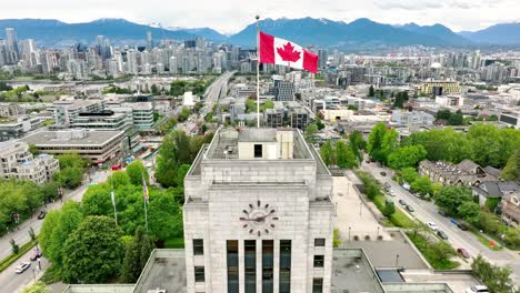 Drone-Se-Eleva-Sobre-El-Ayuntamiento-De-Vancouver-Con-Bandera-Ondeante-En-Vancouver,-Columbia-Británica,-Canadá