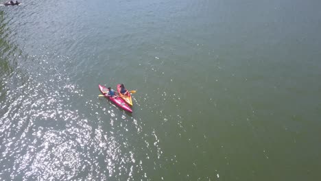 Gente-En-Kayaks-Y-Nadando-En-Un-Lago-Cálido-Con-La-Luz-Del-Sol-Brillando-En-La-Superficie-Del-Agua
