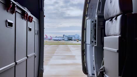 Vista-Del-Pedestal-Hacia-Abajo-Desde-El-Interior-Del-Avión-Con-La-Puerta-Abierta-De-Los-Aviones-Estacionados-En-El-Aeropuerto-Gatwick-De-Londres-En-Segundo-Plano-En-Un-Día-Nublado,-Reino-Unido