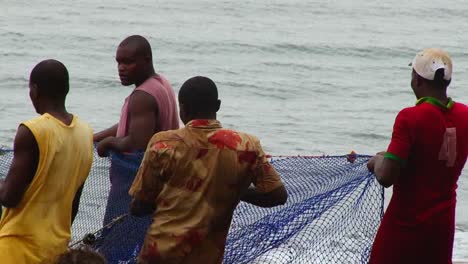 Cuatro-Pescadores-Africanos-Tiran-De-Las-Redes-De-Pesca-En-La-Playa-Después-De-Un-Día-De-Pesca---Cerrar