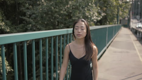 Medium-shot-of-Beautiful-asian-woman-in-black-walking-near-green-railing,-Slowmo