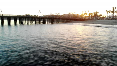 Luftdrohne-Schoss-Bei-Sonnenuntergang-Tief-über-Dem-Pazifischen-Ozean-Vor-Der-Küste-Von-Santa-Barbara-Mit-Stearns-Wharf-Pier-Und-Palmen-In-Kalifornien