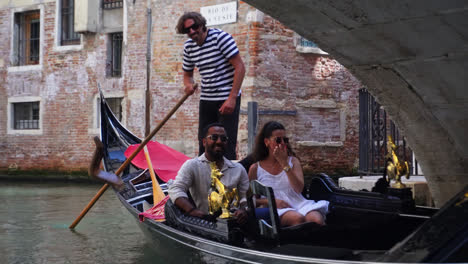 Gondolero-Y-Pareja-De-Turistas-Montando-En-Una-Góndola-Pasando-Por-Debajo-Del-Puente-Arqueado-En-El-Gran-Canal-En-Venecia,-Italia