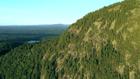 Aerial-drone-shot-flying-over-a-ridge-on-Bore-Mountain-above-thick-green-forest-trees-and-a-blue-lake-in-the-Maine-wilderness