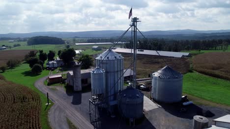 Aerial-push-in-over-cornfields-to-grain-silos-and-rising-up-over-with-view-of-flying-American-flag-at-top-of-silo