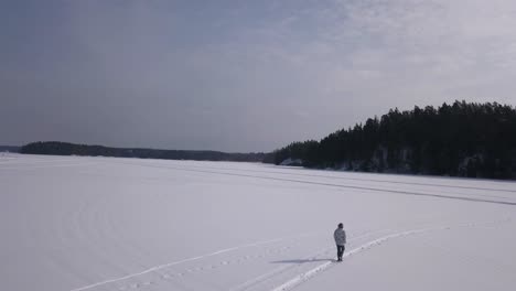 Aerial-shot-of-lonesome-young-woman-walking-on-a-frozen-lake-enjoying-the-great-outdoors