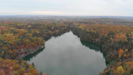 Aerial-footage-over-Pink-Lake-in-Gatineau-Quebec-of-the-lake-with-a-city-in-the-distance-in-autumn