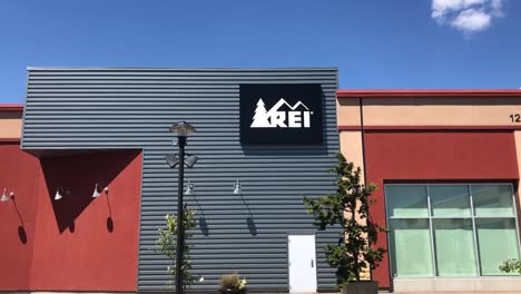 An-Exterior-sign-for-an-REI-outlet-store-in-a-mall-in-the-Pacific-Northwest-on-a-clear,-sunny-day-with-blue-skies-and-minimal-clouds