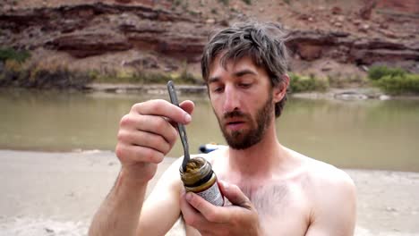 Guy-reading-ingredients-on-sauce-jar-near-river-in-Utah