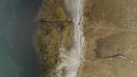 Topdown-aerial-tracking-over-the-edges-of-a-loch-with-autumn-shade-coastline