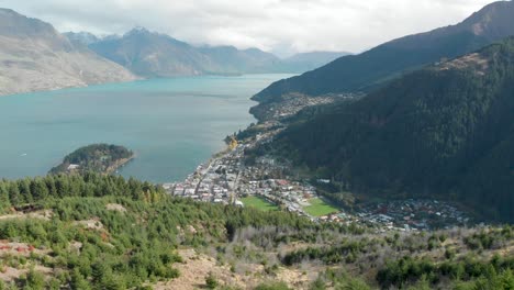 SLOWMO---Beautiful-view-of-Queenstown-from-Queenstown-Hill-track-hike,-New-Zealand-and-Lake-Wakatipu,-mountains-with-fresh-snow,-clouds-and-town---Aerial-Drone