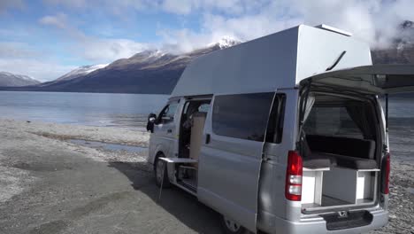 SLOWMO---Motorhome-by-beautiful-blue-Lake-Wakatipu,-Queenstown,-New-Zealand-with-mountains-fresh-snow-cloudy-sky-in-background
