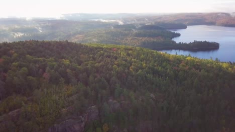 Luftaufnahme-Tagsüber,-Die-über-Herbstwaldfarben-In-Richtung-Ruhiger,-Nebliger-Seen-Fliegt,-Die-Nach-Rechts-Schwenken,-Um-Winzige-Kieferninseln-Und-Reflexionen-In-Kawarthas,-Ontario,-Kanada,-Zu-Enthüllen
