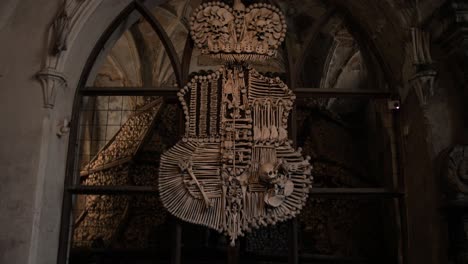 Push-in-shot-towards-coat-of-arms-made-from-human-bones---skull-remains-in-spook-Sedlec-Ossuary-catholic-chapel-in-Czech-republic