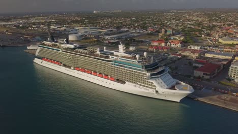 Aerial-establishing-shot-of-the-cruise-ship-in-dock-zooming-out-with-the-island-in-the-background-4K