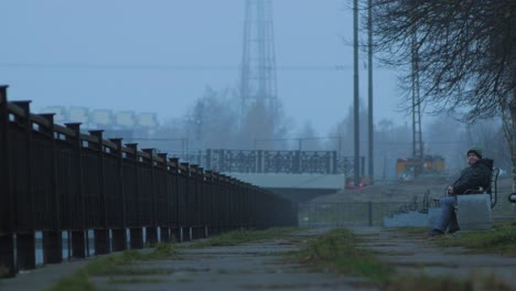 Mature-lady-resting-on-the-bench-near-the-Liepaja-Trade-canal-in-foggy-afternoon,-wide-shot