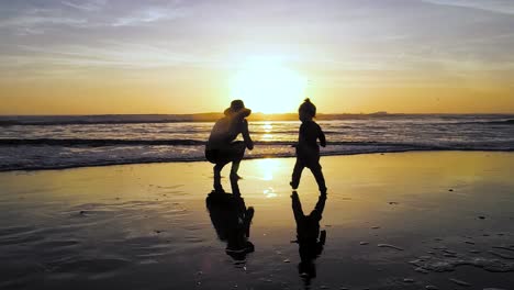 Ein-Kind-Rennt-In-4K-Während-Eines-Atemberaubenden-Sonnenuntergangs-Am-Strand-Mit-Einem-Farbenfrohen-Himmel-Zu-Mamas-Armen