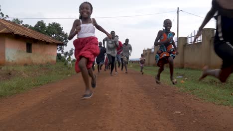 Eine-Gruppe-Afrikanischer-Jugendlicher-Und-Kinder,-Die-Mit-Einem-Lächeln-Im-Gesicht-Eine-Unbefestigte-Straße-Hinunterrennen