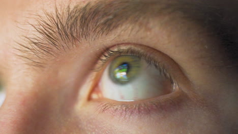 Close-up-macro-view-of-young-man's-eye-moving-fast-staring-at-video-games-and-the-bright,-flashing-screen-of-a-computer-with-vivid-lights-and-colors