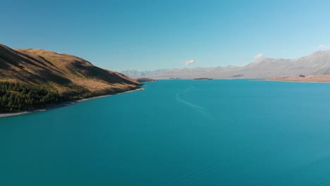 SLOWMO---Aerial-shot-of-Lake-Tekapo,-New-Zealand-and-its-Beautiful-Turquoise-Blue-Water-wiht-mountains-in-background