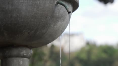 Tilt-up-shot-of-a-narrow-stream-of-water-falling-from-a-fountain-in-slow-motion-in-Granada,-Spain