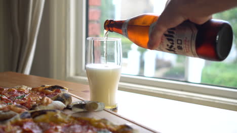 Mann-Gießt-Asahi-Bier-In-Ein-Glas,-Während-Er-Pizza-Isst