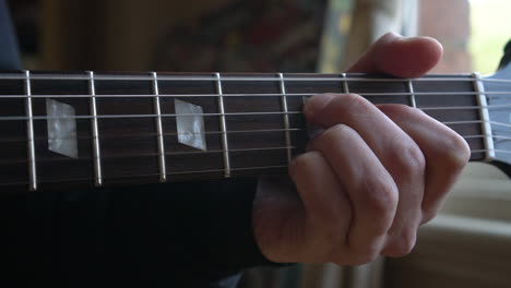 Man-Practising-a-vintage-black-electric-guitar,-rehearsing-chords,-solos-and-octaves-in-a-natural-light-environment.